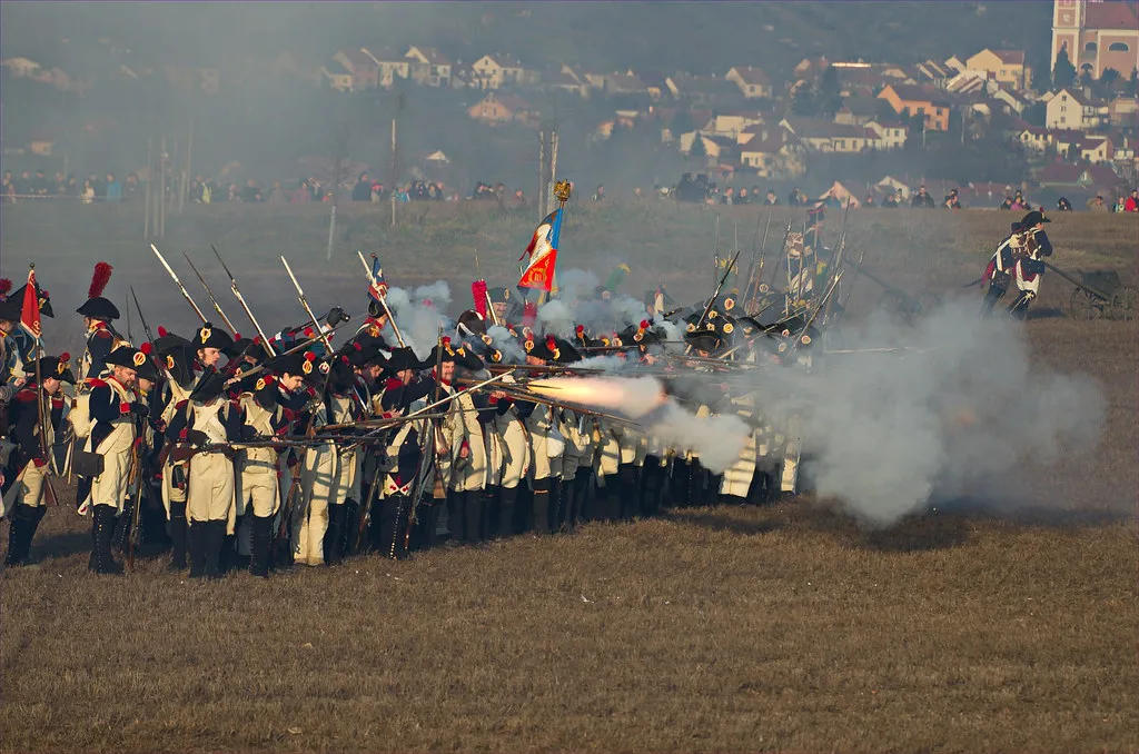 Reenactors in Napoleonic uniforms firing muskets at a Battle of Austerlitz reenactment