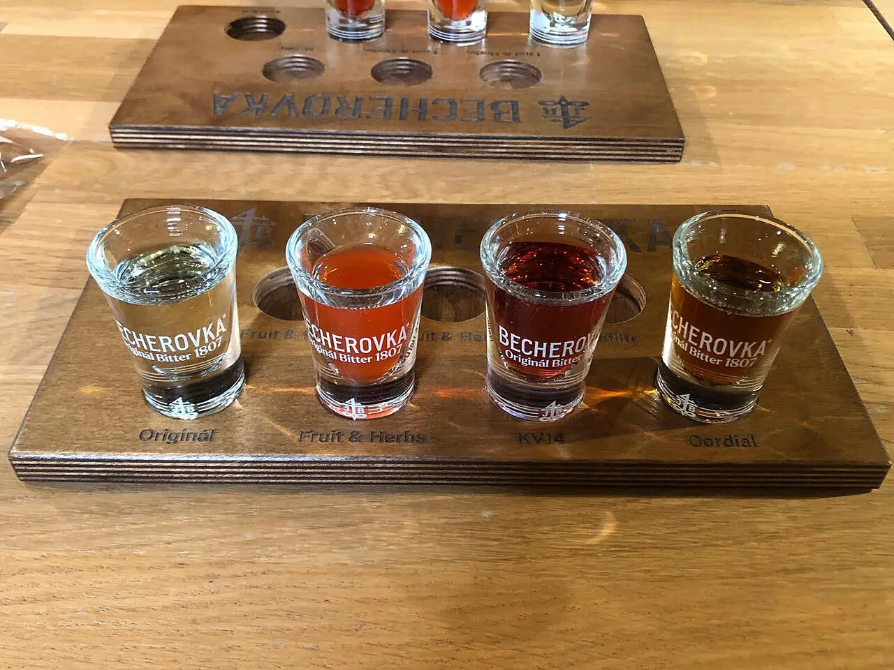 A Becherovka tasting flight of four shot glasses on a wooden board.