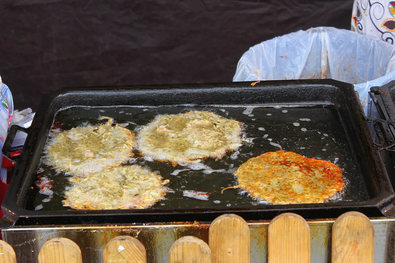 Bramboráky potato pancakes frying on a griddle at a food stall.
