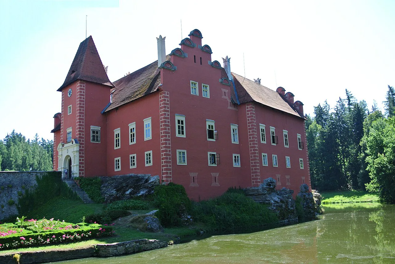 The red facade of Červená Lhota Castle above the water.