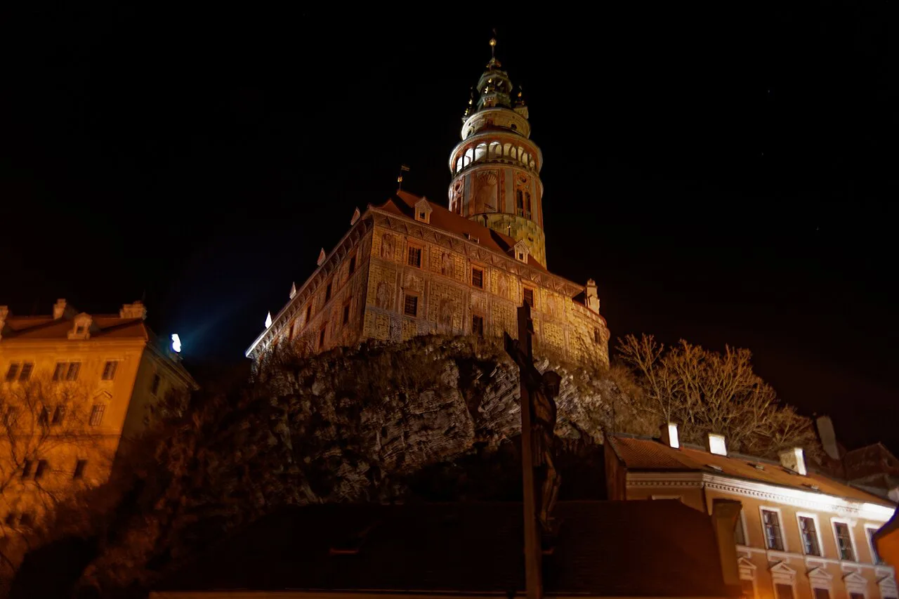 Český Krumlov Castle tower lit up at night, seen from the Barber's Bridge.