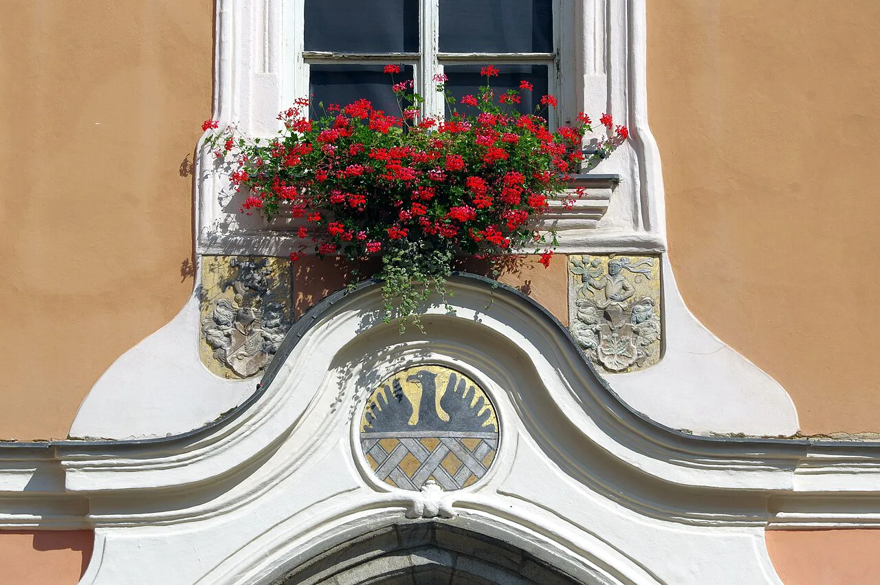 Window with flower box and coat of arms on a building in Cheb