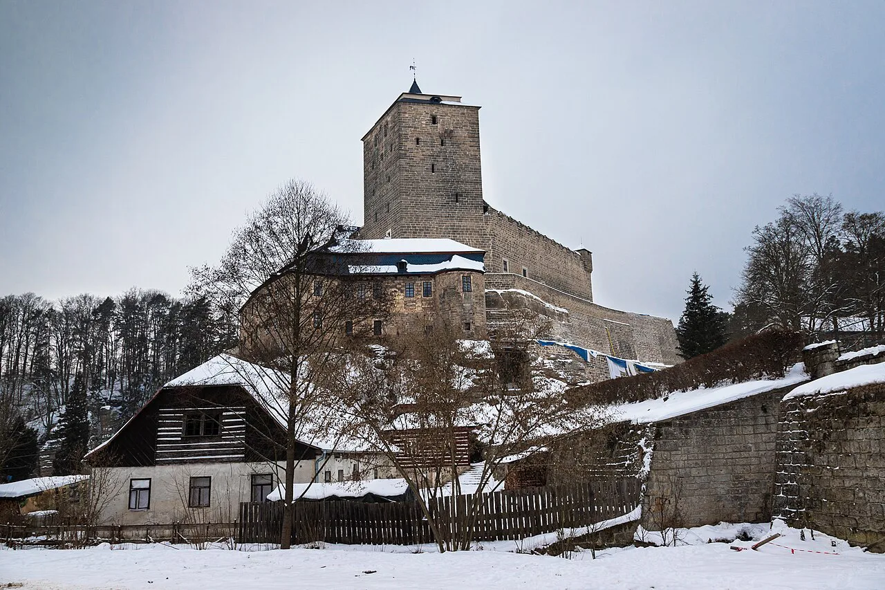 Kost Castle in winter, with snow on the roofs below.