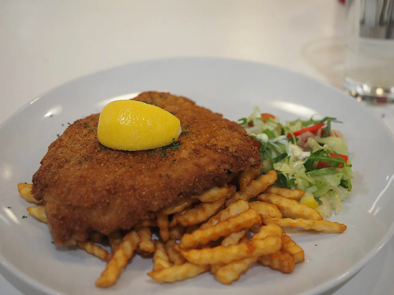 A breaded schnitzel with lemon, fries and salad.
